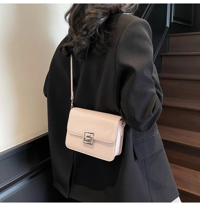 Detail view of a beige square leather crossbody bag with metallic clasp on a black blazer