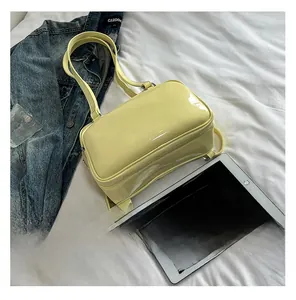 Detail of pale yellow glossy leather handbag with silver hardware on white bedding