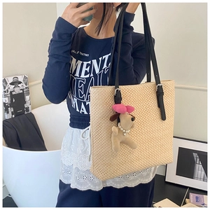 Detail of light beige woven tote bag with black leather straps and plush dog charm