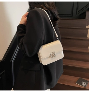 Detail of cream patent leather crossbody bag with silver geometric buckle and shoulder strap