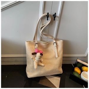 Detail of straw tote bag with cream leather straps and a cute plush puppy charm