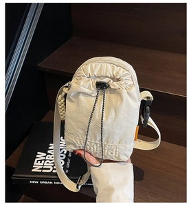Close-up of cream nylon crossbody bag with drawstring closure and brand embroidery detail