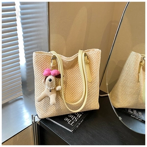 Detail of beige straw tote bag with thin leather straps and a plush puppy charm
