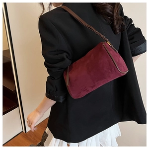 Chic burgundy suede handbag with brown leather trim worn by model in minimalist setting