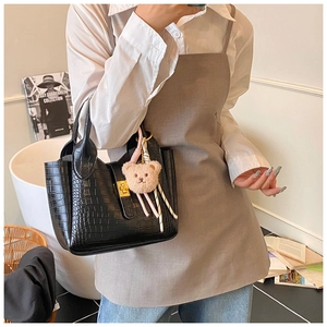 Details der schwarzen Handtasche mit Krokodilstruktur, Goldschnalle und Bärenanhänger
