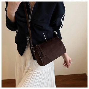Detail of a dark brown suede cylinder crossbody bag styled on a female model