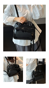 Detail view of black glossy patent leather handbag with silver zippers and multi-way straps
