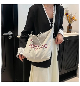 Detail of white tote bag featuring purple lettering and adjustable bow tie strap