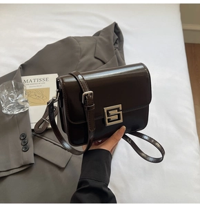 Detailed close-up of a dark coffee square bag with silver S-clasp on a grey blazer