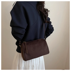 Detail of dark brown suede crossbody bag styled with a blue sweater and white pleated skirt