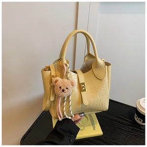 Detailansicht der gelben Eimer-Tasche mit Krokodilmuster, Bärchen-Anhänger und Metallschnalle