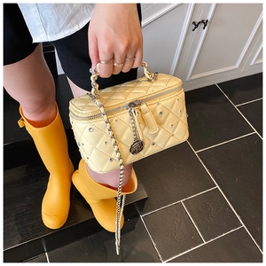 Detail of yellow quilted box bag featuring silver rivets and a metal rose charm