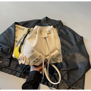 Detail of beige bucket bag with drawstring closure, metal eyelets and elephant charm