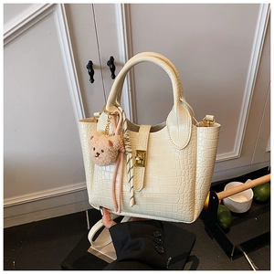 Detailansicht der cremefarbenen Krokodil-Eimertasche mit Goldverschluss und Bärenanhänger