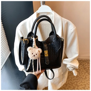Detail der schwarzen Beuteltasche mit Krokoprägung, Goldverschluss und Plüschbär-Anhänger