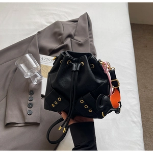 Detail of black leather bucket bag with drawstring closure and orange elephant charm