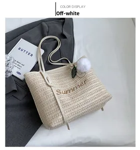 Detail shot of a cream straw tote bag with Summer embroidery and plush ball charm