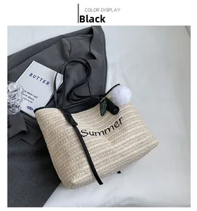 Detail of woven straw tote bag with Summer embroidery and black leather straps