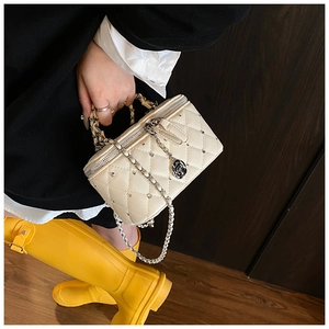 Detail of cream quilted crossbody bag with silver studs and rose charm on a model