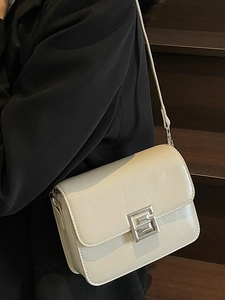 Minimalist beige rectangular crossbody bag with silver metal lock on a black outfit