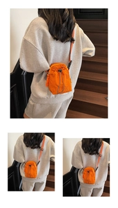 Detail view of bright orange drawstring crossbody bag with adjustable strap and embroidery