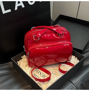 Detail view of red glossy patent leather handbag with dual zipper design and shoulder strap