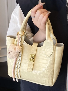 Elegante gelbe Beuteltasche mit Krokodilprägung, Goldschließe und rosa Bärenanhänger