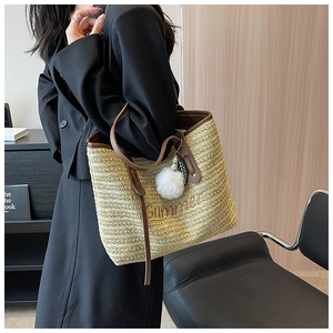 Close-up of woven straw tote bag with Summer embroidery and brown leather handle
