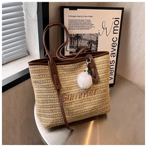 Detail of straw tote bag featuring Summer embroidery, brown leather straps and pompom