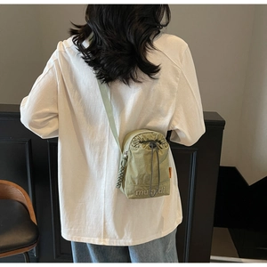 Rear view of a light green canvas drawstring crossbody bag worn by a casual model