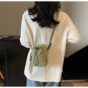 Detail of army green nylon drawstring crossbody bag with embroidered logo on a table