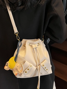 Chic cream drawstring bucket bag with a bow accent and cute elephant charm on a model