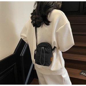 Detail of black nylon crossbody phone bag with orange label and drawstring closure