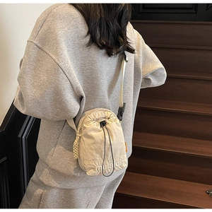 Detail of cream nylon crossbody bucket bag featuring drawstring closure and logo embroidery
