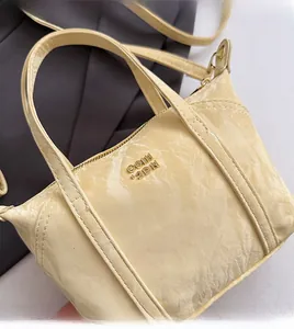 Gros plan du mini sac cabas jaune crème avec texture vernie plissée et logo doré