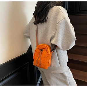 Close-up of bright orange drawstring crossbody bag with logo on gray hoodie