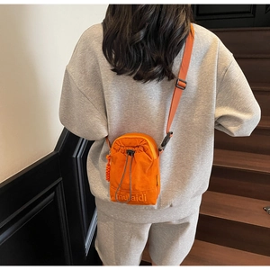 Detail of orange canvas drawstring crossbody bag with embroidered logo on a model