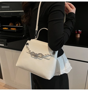 Close-up of a white leather crossbody bag featuring a silver metal bow and chain detail