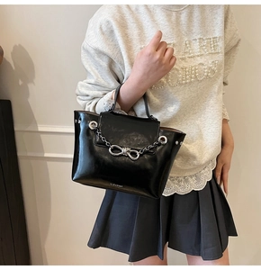 Detail of black glossy crossbody bag with silver bow buckle and chain held by model