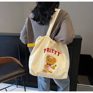 Detail of a beige tote bag with red PRETTY embroidery and a cute teddy bear cartoon