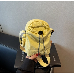 Detail of light yellow nylon crossbody bag featuring drawstring closure and side orange tag