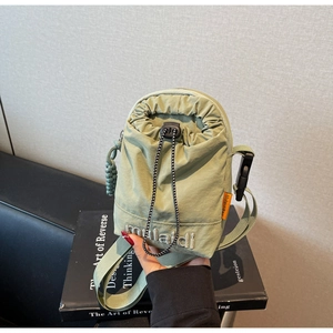 Close-up of light green nylon drawstring crossbody bag with embroidered logo and orange tag