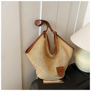 Close-up of beige straw woven tote with brown leather handles and decorative pendant