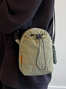 Olive green nylon drawstring crossbody bag with embroidered logo and braided charm detail