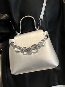 Metallic silver crossbody bag with metal chain and bow detail over a black coat
