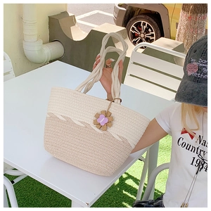 Detailed texture of two-tone woven straw tote bag with floral charm in outdoor setting