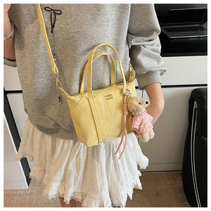Détail du mini sac jaune clair avec texte COIN KISS, breloque ours et bandoulière