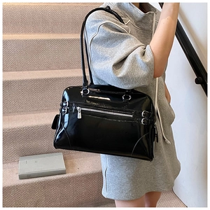Model wearing a glossy black patent leather underarm bag with silver hardware on stairs