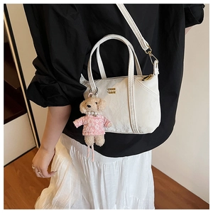 Détail du mini cabas blanc avec logo doré et charm d'ours en peluche sur le mannequin