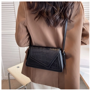 Detail view of black crocodile pattern crossbody bag worn over a brown jacket